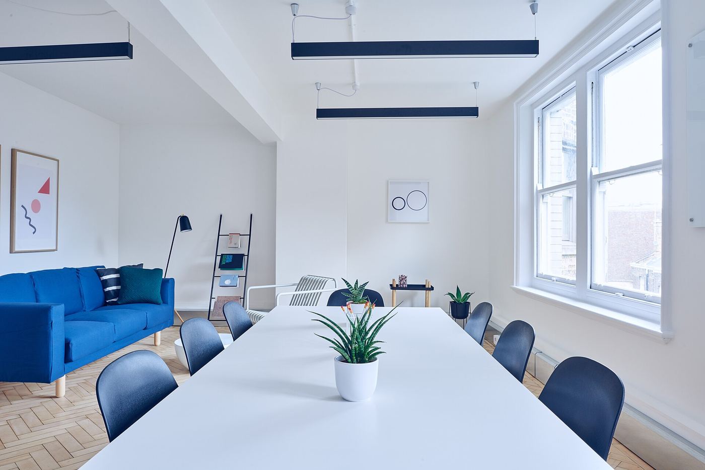 White office with a long meeting table and a blue sofa